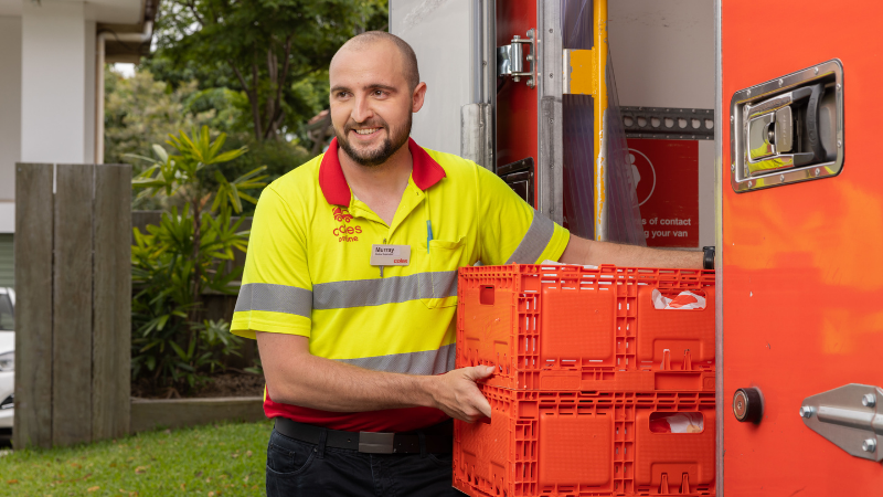 A male team member unloading two crates from a Coles delivery truck 