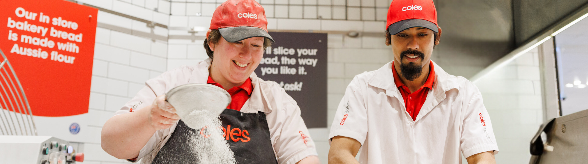 Male and female Coles Bakers sifting flour  kneading dough in the bakery, wearing a red cap, white uniform 