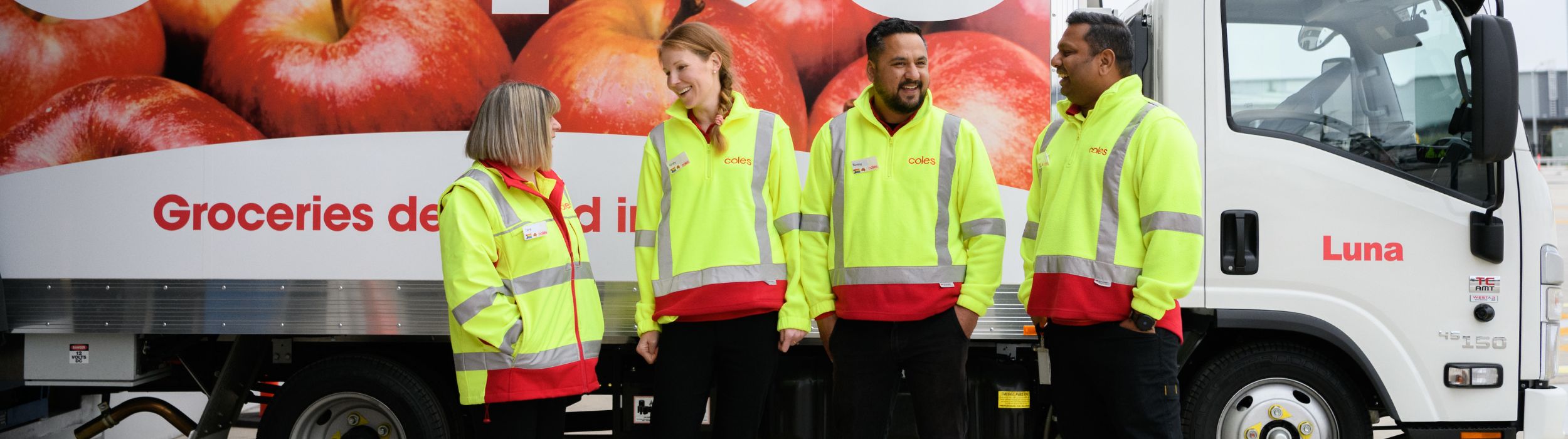 Four Male and female delivery drivers having a conversation at the loading dock at the CFC in front of a Coles branded delivery van