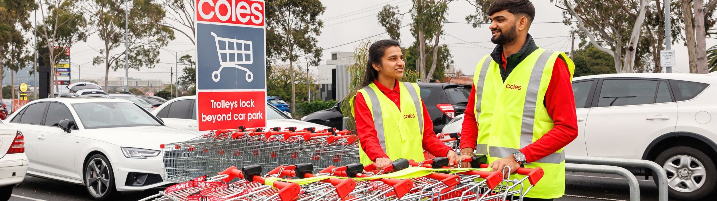 Two Coles employees pushing trolleys into a vehicle in the Coles parking lot