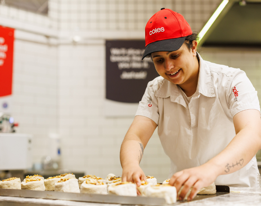 A female Coles Baker is seen preparing dough. She is wearing a Coles branded red cap and white uniform