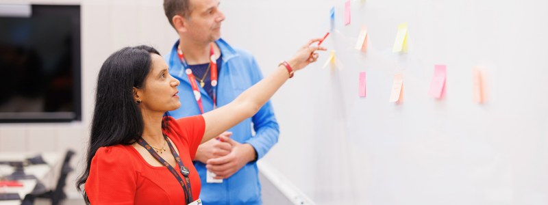 A female and male team member adding post-it notes to a whiteboard in the Coles Store Support Centre