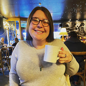 Woman with brown hair smiling and holding a mug