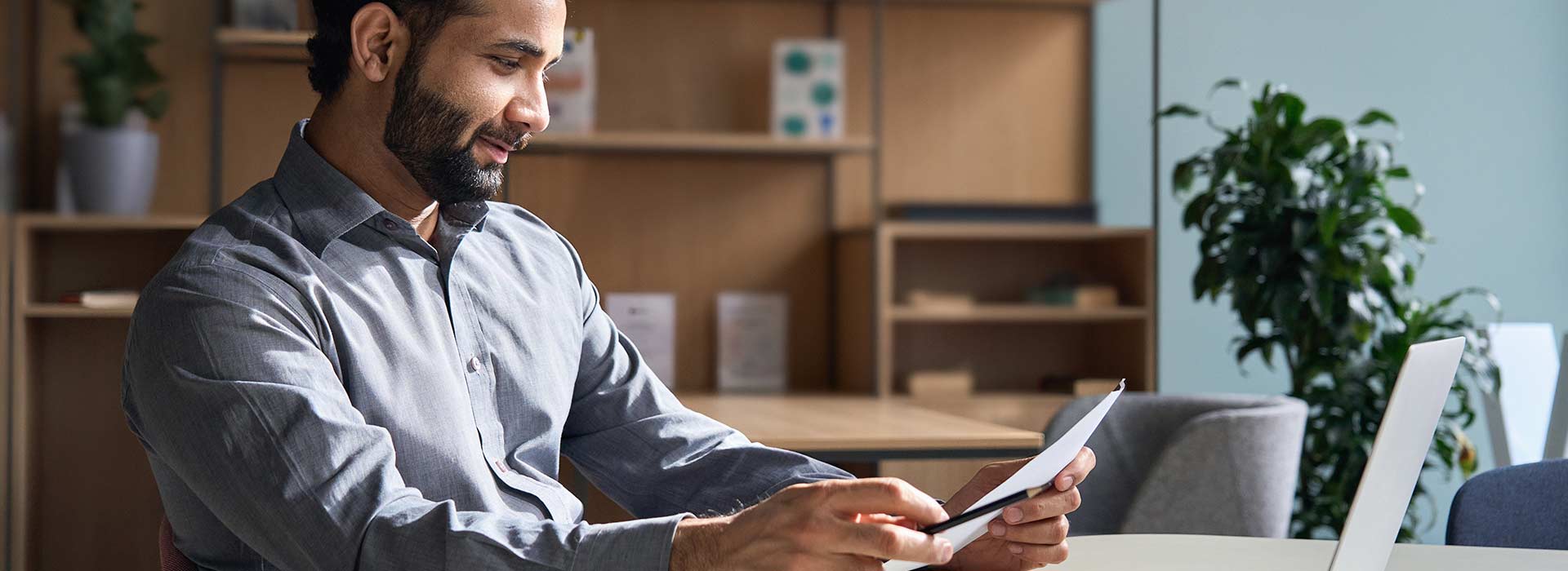 Man wearing shirt and reading peice of paper in home office