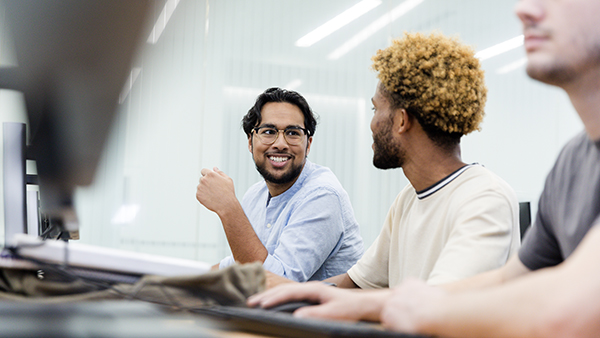 Three young men working at a computer station.