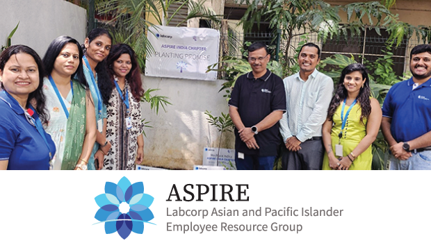 A group of ASPIRE India Chapter members stand outdoors at the MSR Vaishnavi Office in Bengaluru, surrounded by greenery and signs reading “ASPIRE INDIA CHAPTER PLANTING PROMISE.”