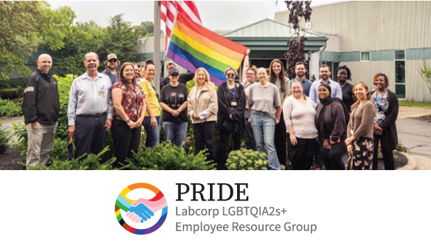 A group of PRIDE ERG members gather around a flagpole in front of a building, raising the Pride flag alongside the American flag during Pride Month.