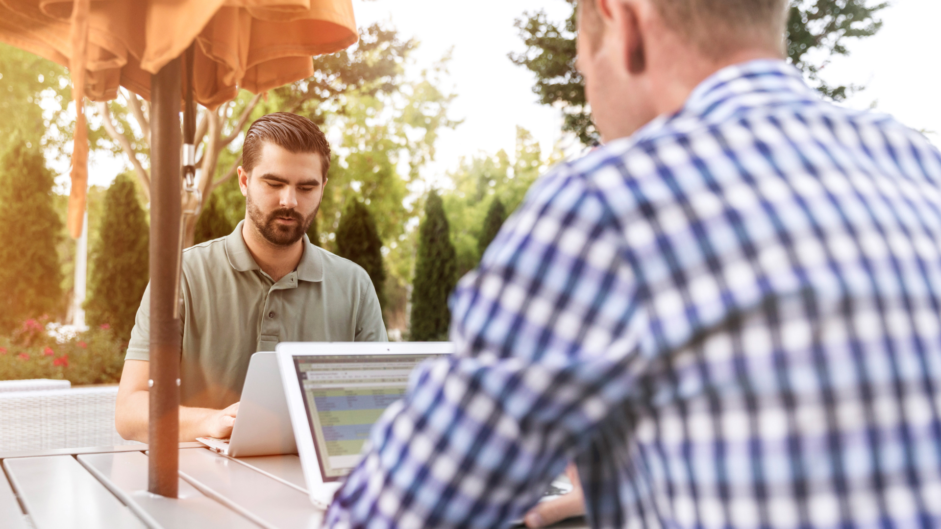two men working on laptops outdoors on picnic table