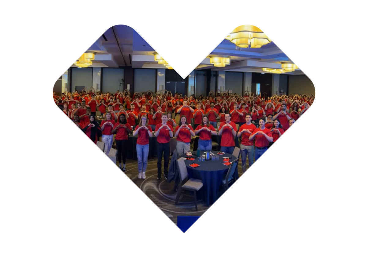 A large group of people, mostly dressed in red shirts, are posing for a photo indoors. Many of them are making heart shapes with their hands. Behind the group, silver balloons spell out "LDP" and red and white balloons are arranged together.