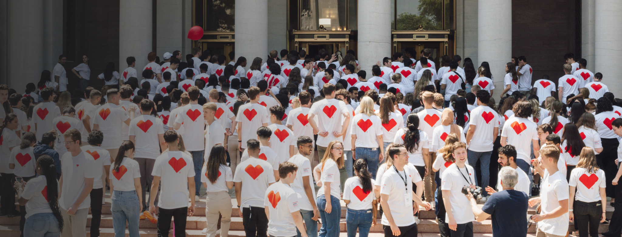 Group of CVS Health interns wearing white shirts with red heart logos gathered outside a campus building.