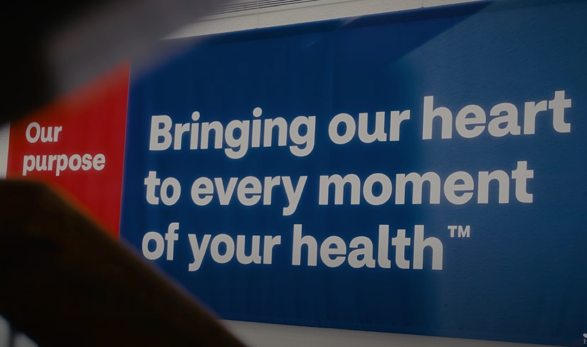 A blue and red sign displays the text: "Our purpose - Bringing our heart to every moment of your health™." The text is white, with "Our purpose" on the red section and the rest on the blue section.