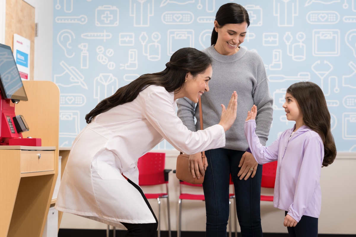 A healthcare professional in a white coat high-fives a young girl while the girl