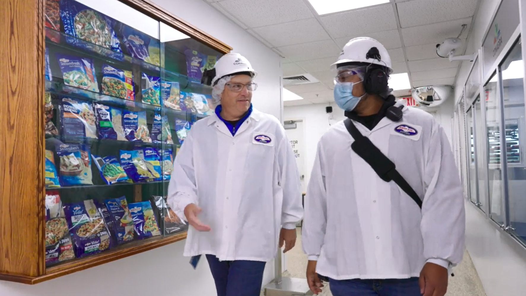 Two Darien employees walk down a hallway with Birds Eye products in a glass cabinet on the wall