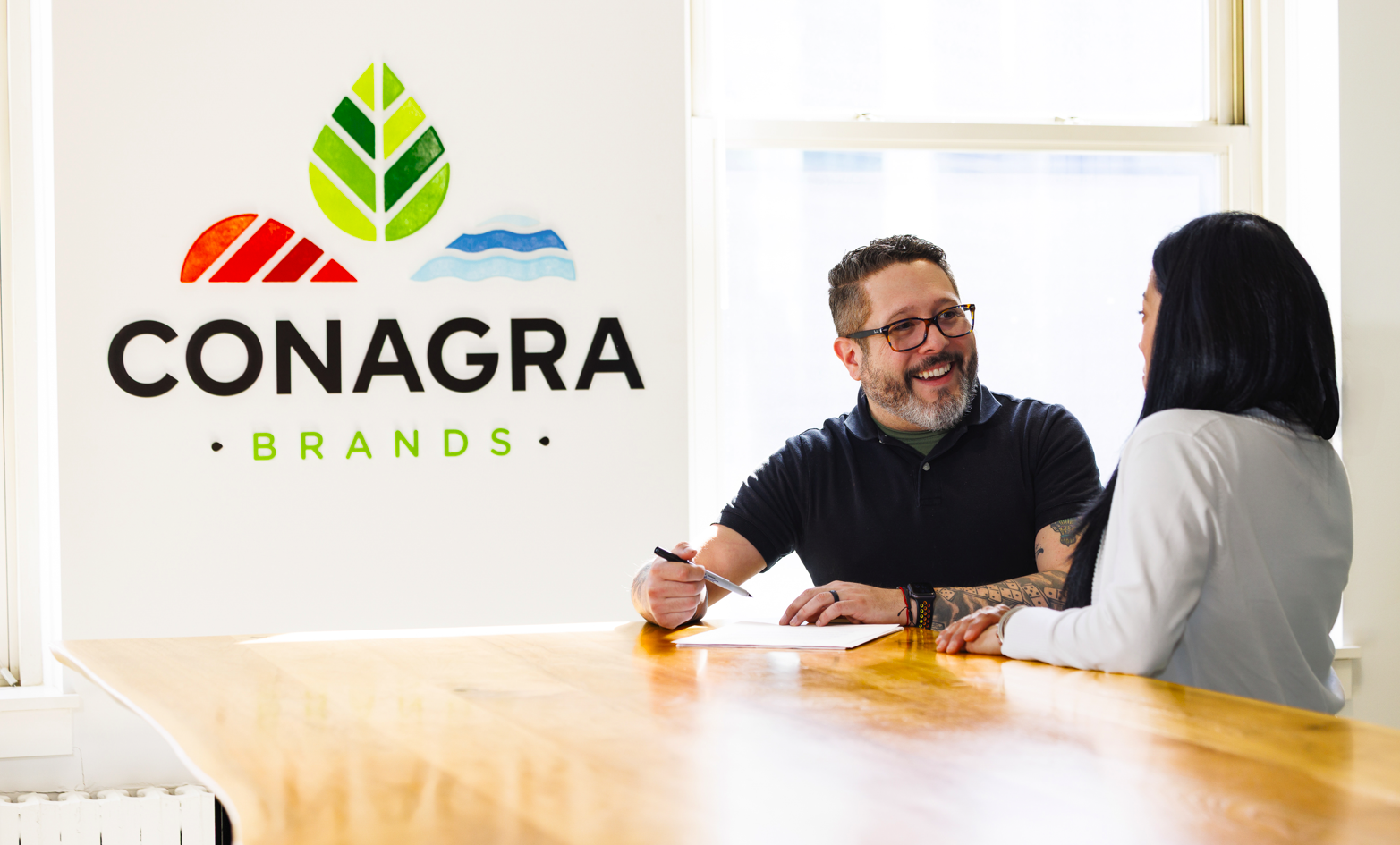 Two employees chat next to a table with the Conagra logo in the background