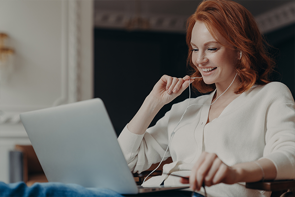 redhead woman has a conversation on a laptop using earphones
