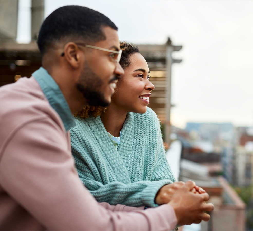 two people look out to the city leaning on a ledge on the roof