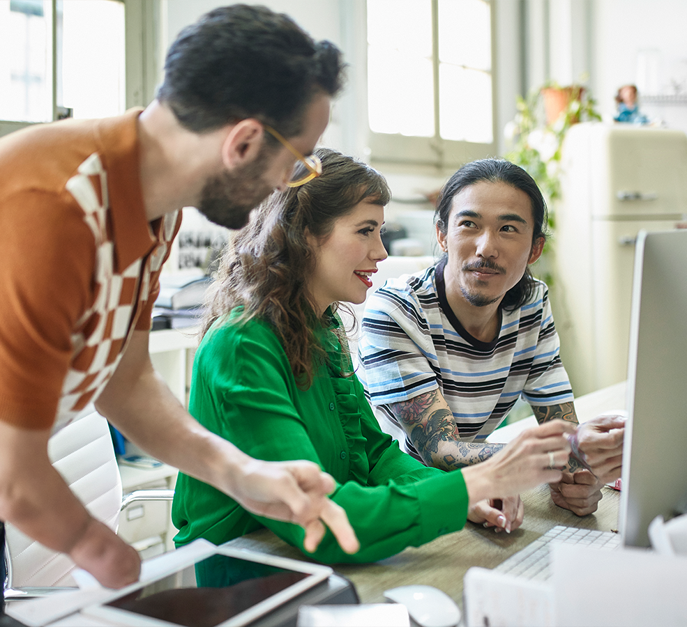 three people have a discussion in an office in front of one computer screen