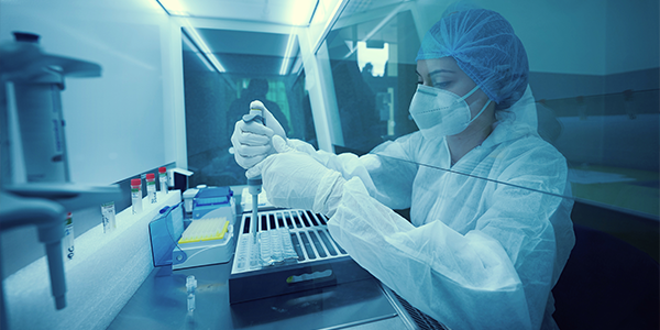 a female scientist wearing full protective gear, pipetting into a tray from behind a protective glass shield