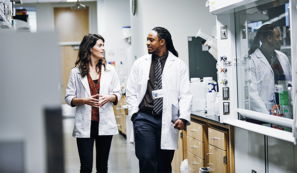 two scientists in white coats walk down the hall in a laboratory