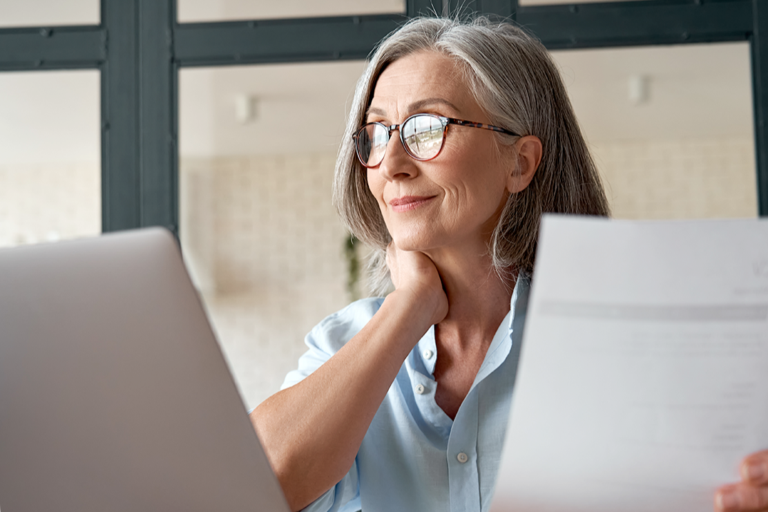 woman sitting in front of a laptop holding a piece of paper