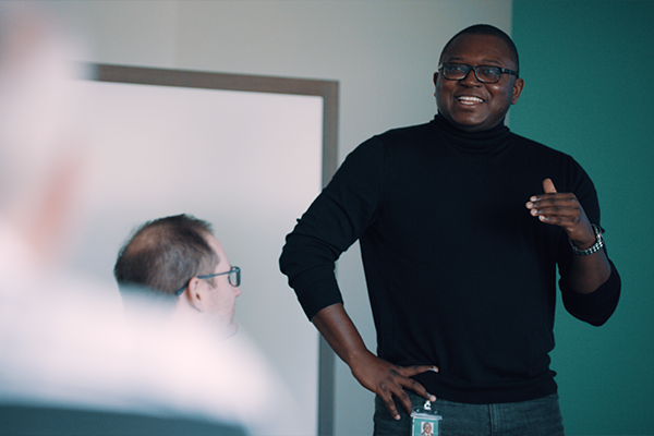 a man standing in a conference room speaking to others who are seated
