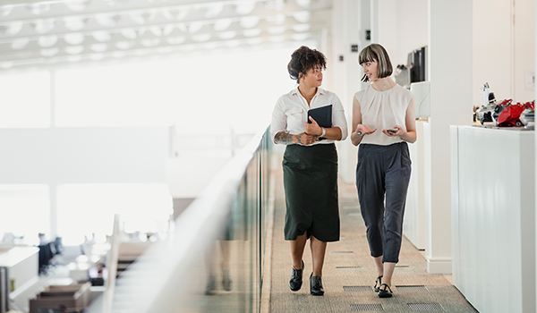 two women walking down an open hall in an office talking