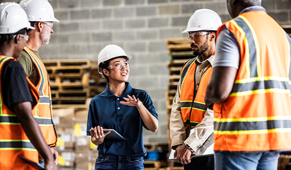 Female warehouse supervisor speaking with a group of employees