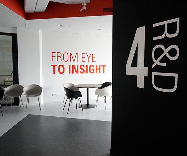 picture of interior of a modern-style office, with a sitting area with tables and chairs and a sign that says 4: R&D