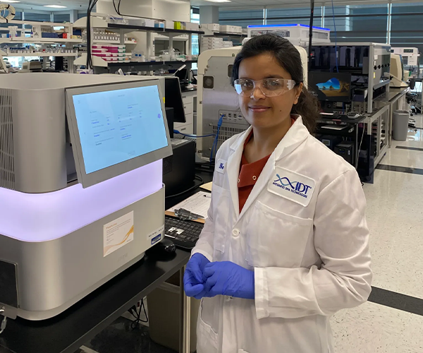 a female scientist in a white coat, gloves and safety glasses standing inside of a lab