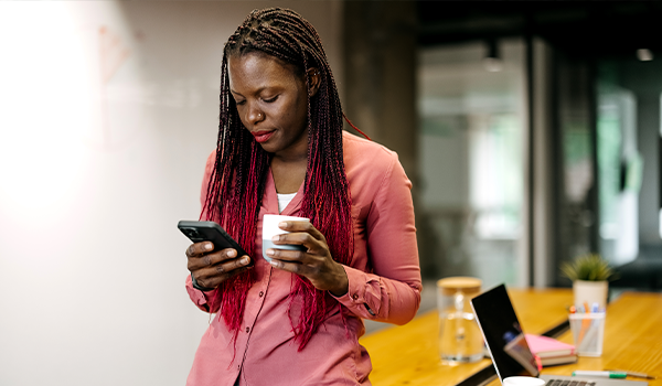 woman holding a cup in one hand, uses her phone in the other
