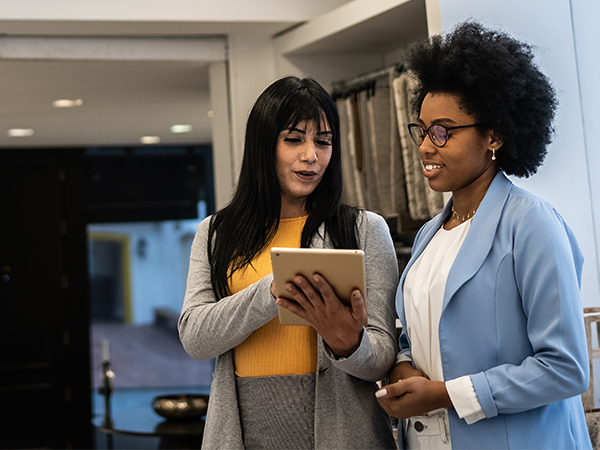 two women look at a tablet in an office