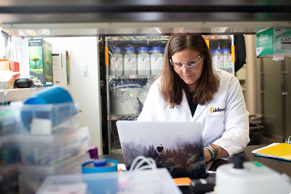 woman working on a computer in a lab wearing an Aldevron lab coat