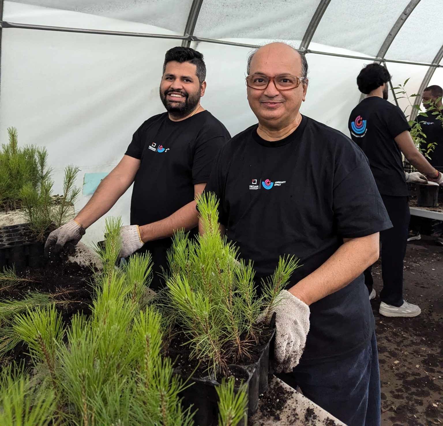 Two Trojan Technologies employees smile as they prepare tree saplings for planting at a volunteer event