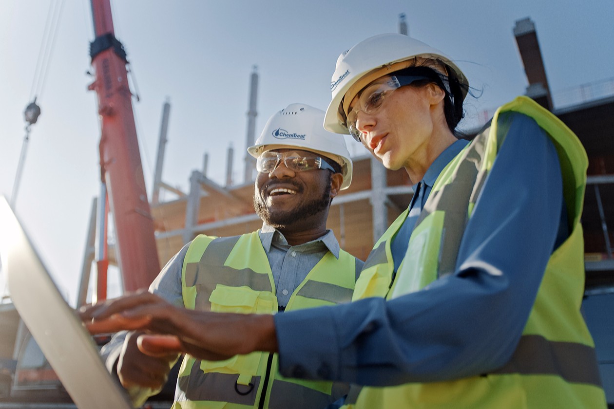 Two ChemTreat field service technicians in hardhats and work vests consulting at a customer site