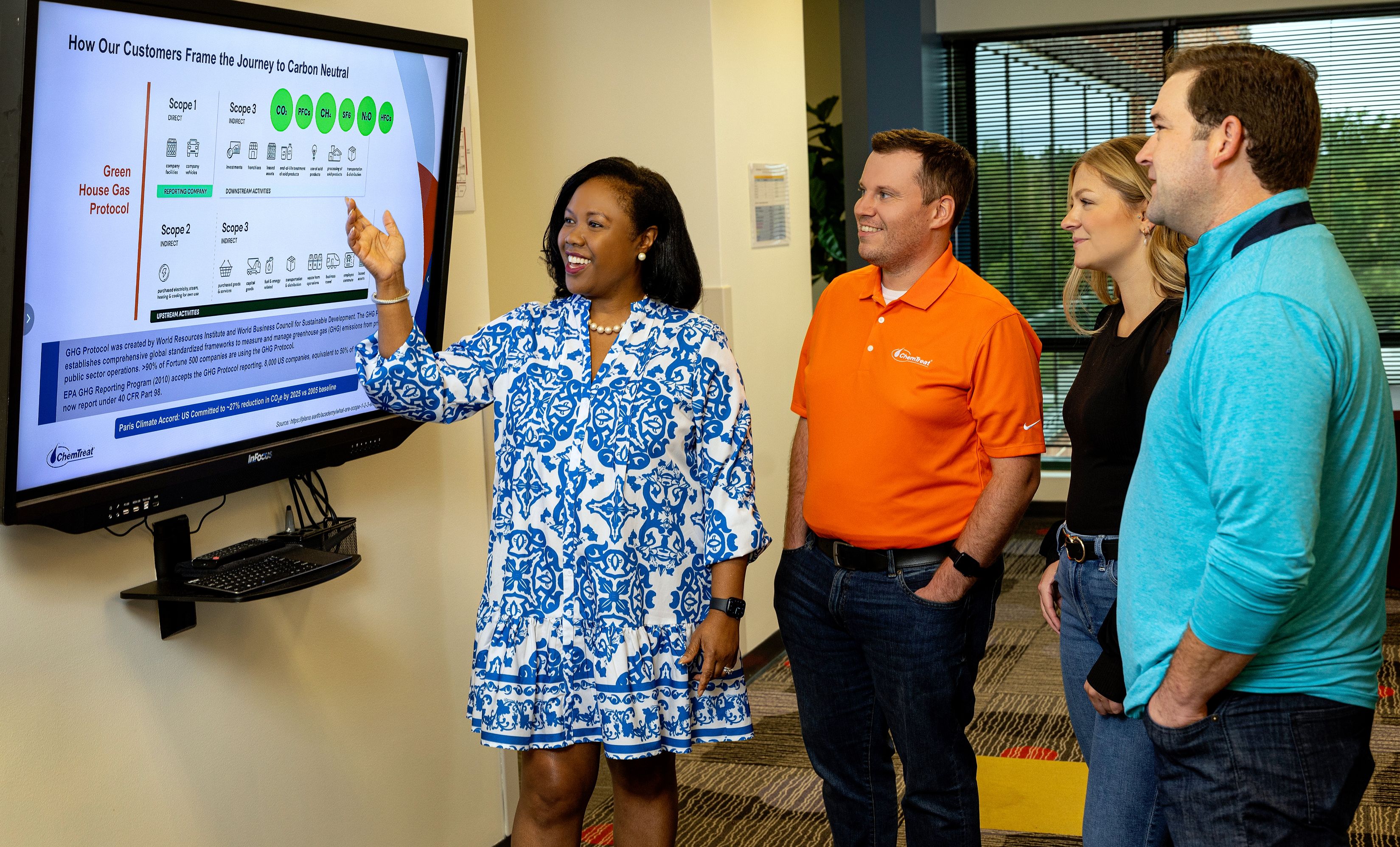 Four ChemTreat associates smiling and discussing a daily management dashboard on a screen