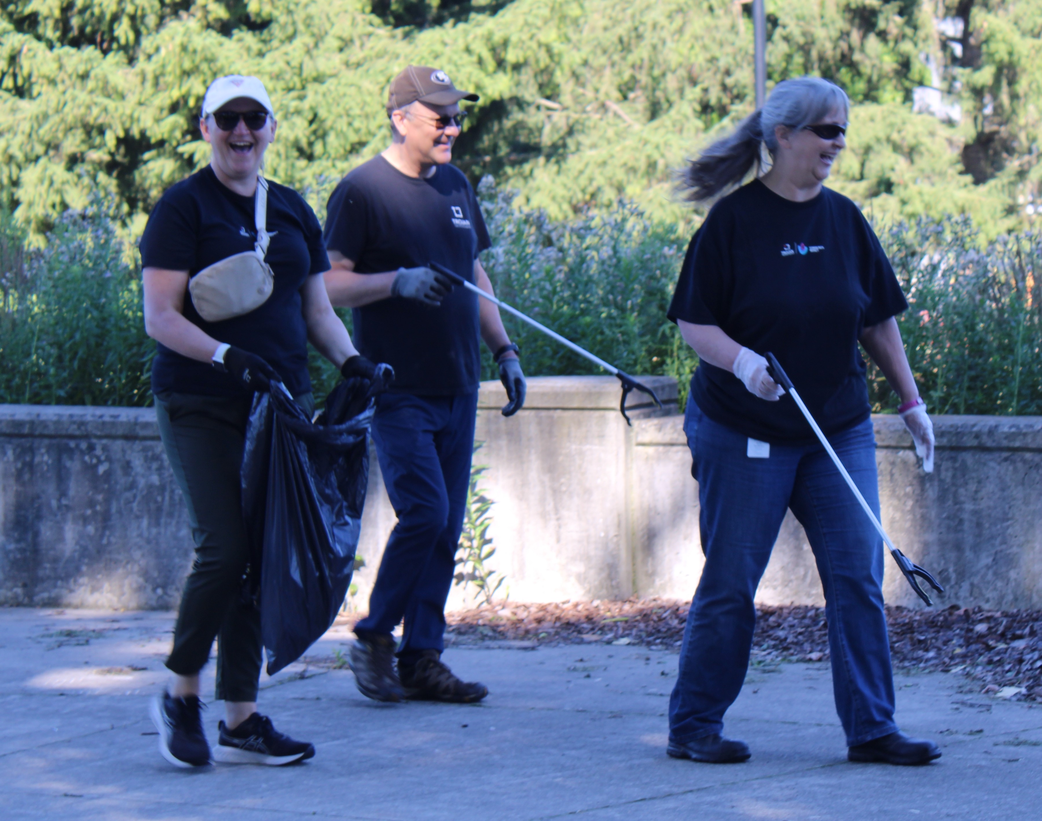 Three Trojan Technologies employees smile as they pick up trash at a community cleanup event