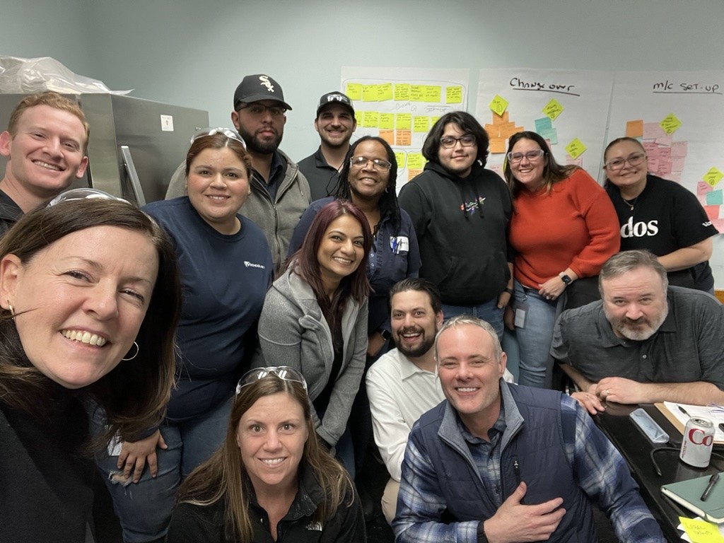 Videojet and Veralto team members smile for a selfie in front of a white board with post-it notes