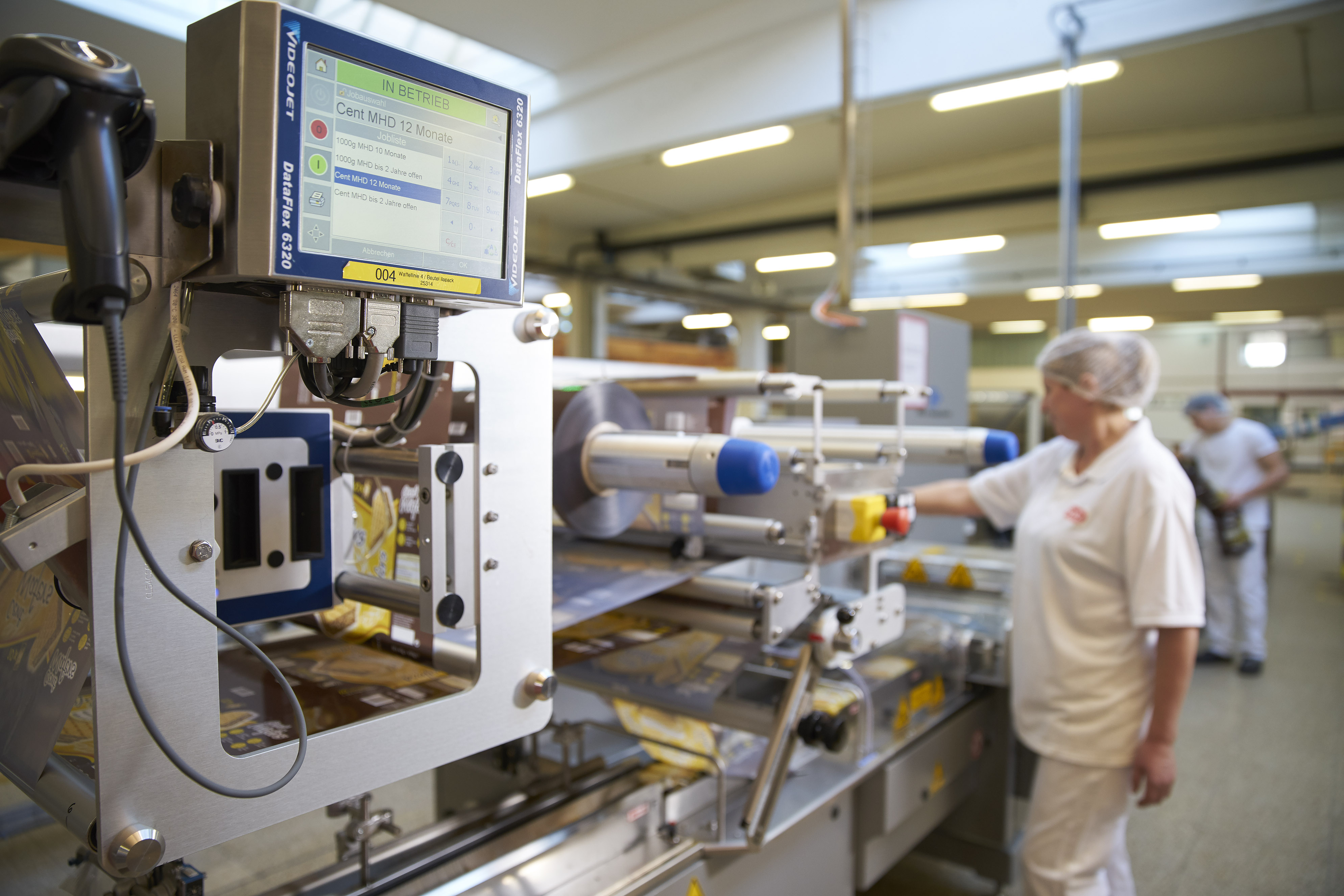 A factory worker monitors packaging being marked and coded by a Videojet printer