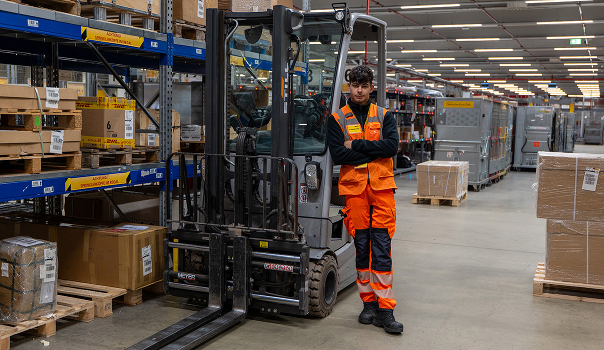 Azubi Fachkraft für Lagerlogistik steht angelehnt an einen Gabelstapler