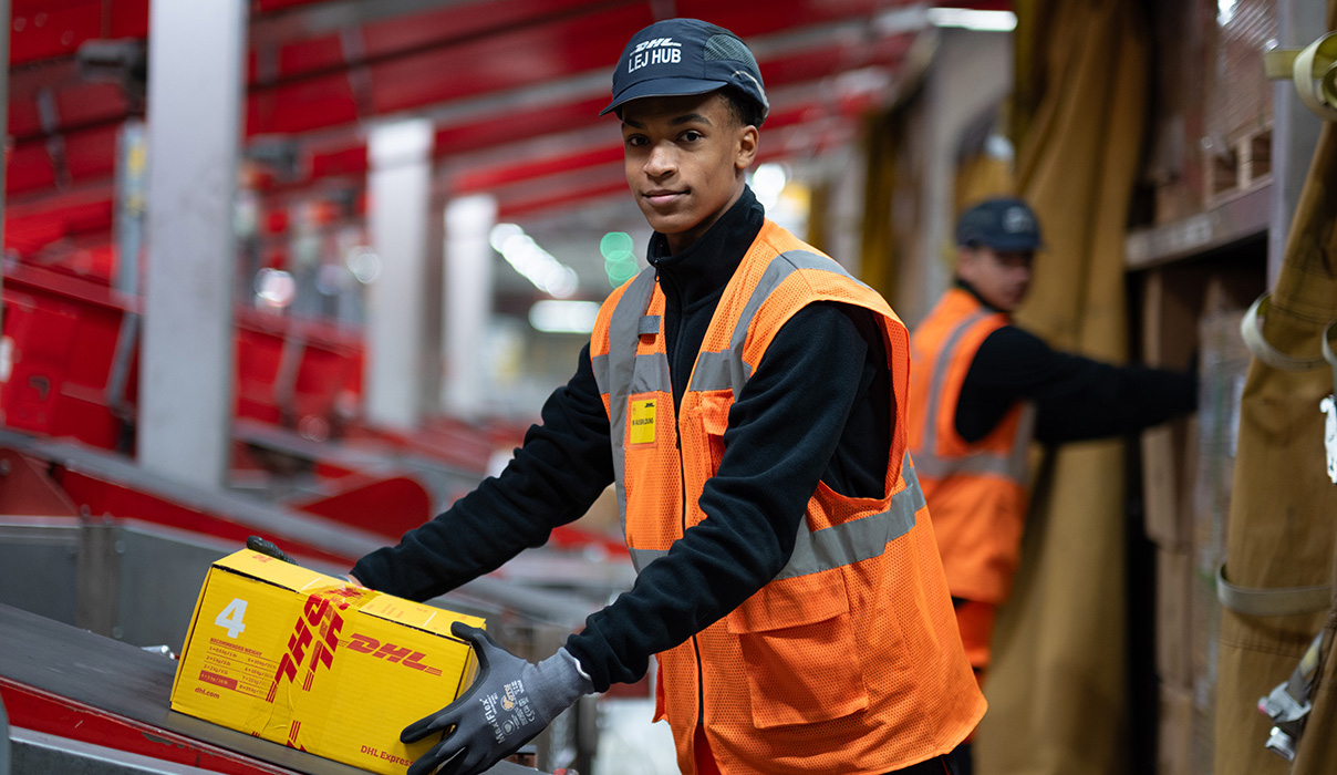 Azubi Fachpraktiker Lager legt ein DHL Paket auf das Förderband