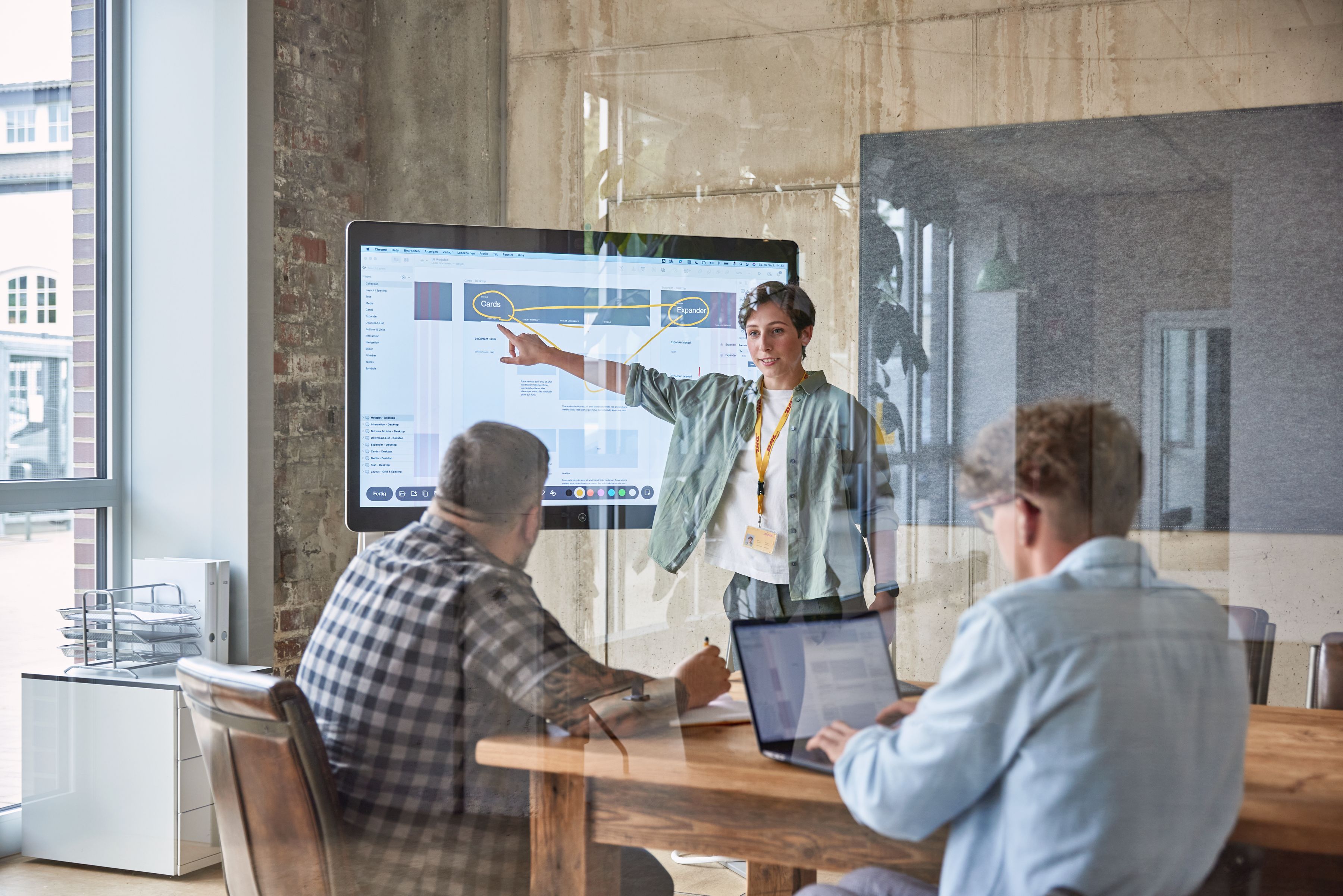 Three people in a meeting, with one of them presenting.
