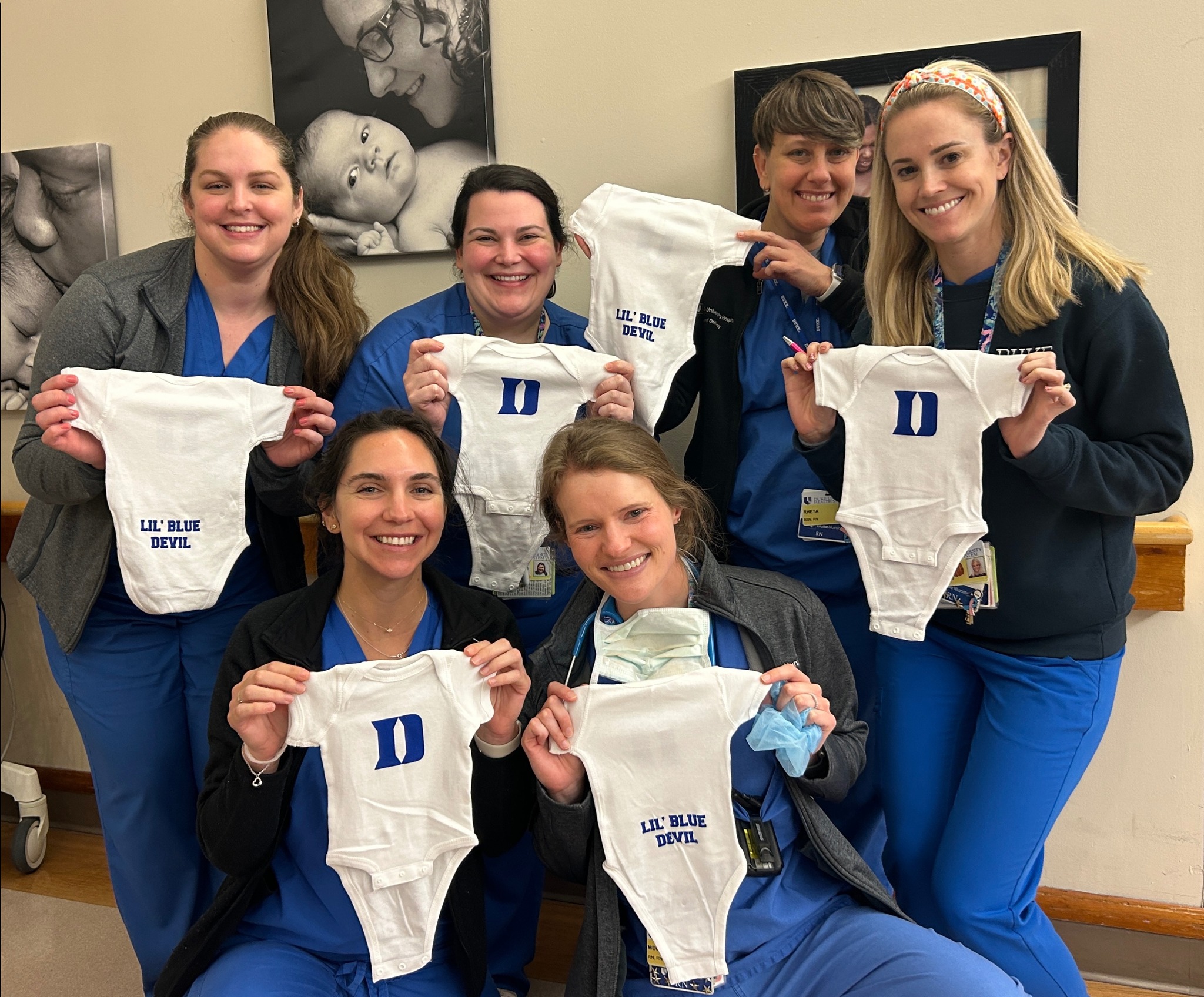 group of nurses smiles holding up duke onesies. 