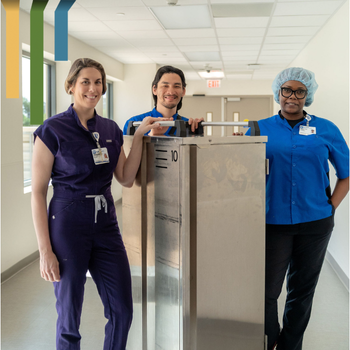 Three team members smile with a food service cart in a hospital hallway.