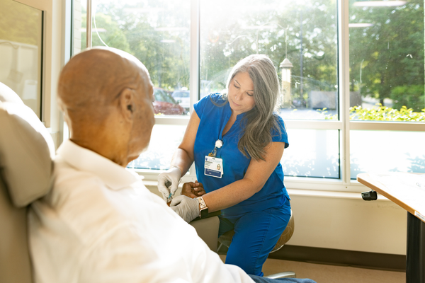 Female nurse in blue scrubs helps a cancer patient with a treatment.