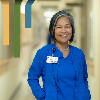 Female team member smiles in blue scrubs in a hospital hallway.