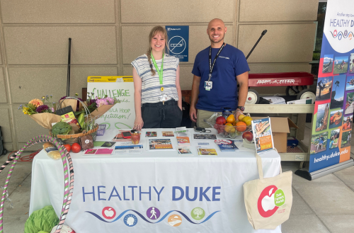 Team members smile at the Farmer's Market in a booth promoting healthy living.