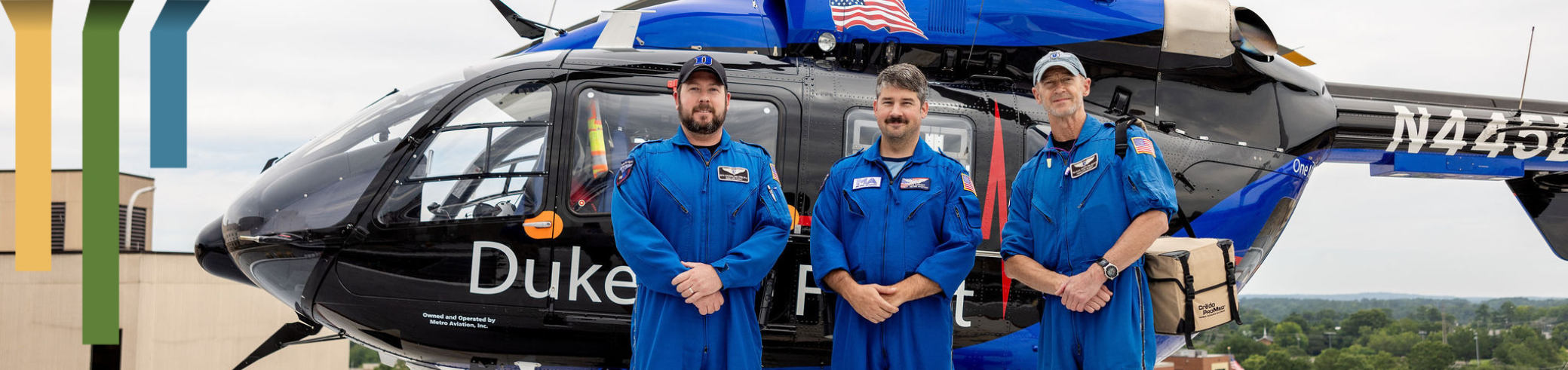 Three team members smile in front of a Duke Life Flight helicopter.