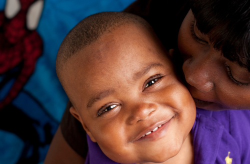 small boy smiles as his mother kisses him.