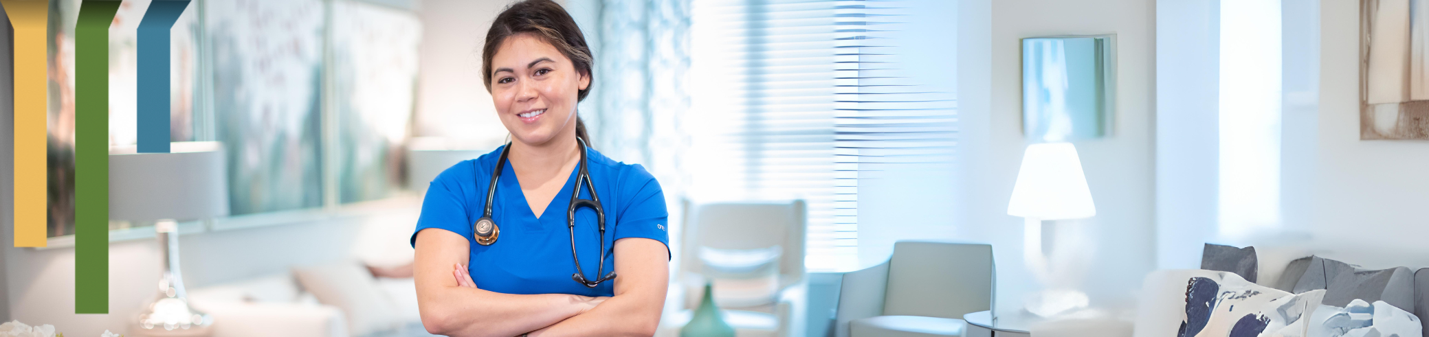 Female nurse smiles in blue scrubs in patient home.