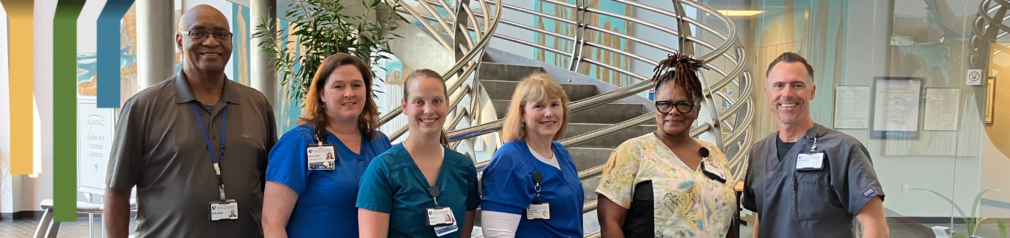 Group of team members in scrubs and business casual attire smile together.